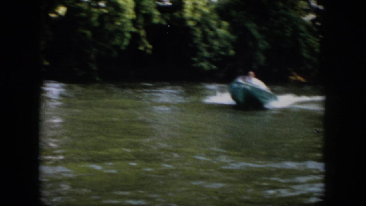 1958 Virginia home-movie frame showing a small blue speedboat moving away along a tree-lined river.