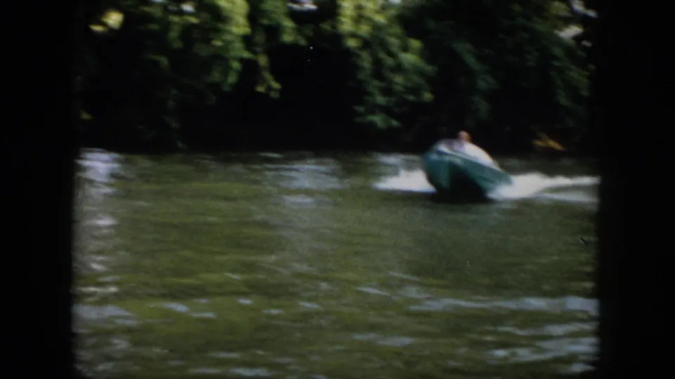 1958 Virginia home-movie frame showing a small blue speedboat moving away along a tree-lined river.