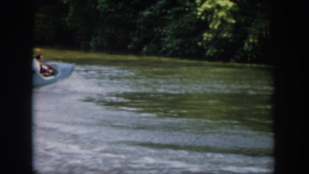 1958 Virginia frame showing the small speedboat moving away toward a shaded tree-lined bend in the river.