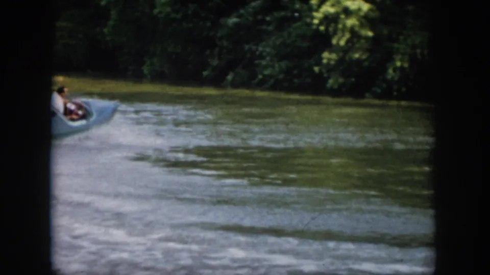 1958 Virginia frame showing the small speedboat moving away toward a shaded tree-lined bend in the river.