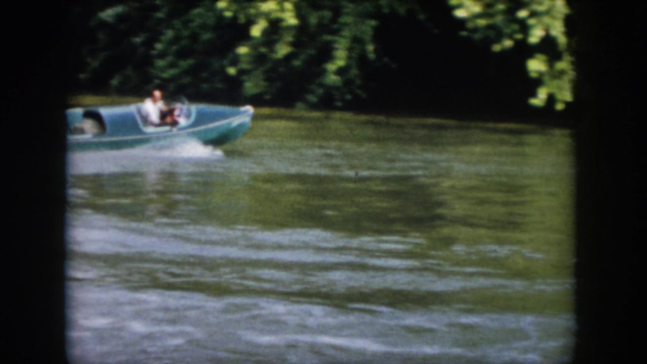 1958 Virginia 8mm frame showing a small motorboat moving across a tree-lined river, with a man visible aboard.