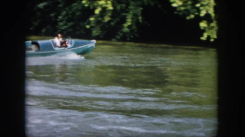 1958 Virginia 8mm frame showing a small motorboat moving across a tree-lined river, with a man visible aboard.