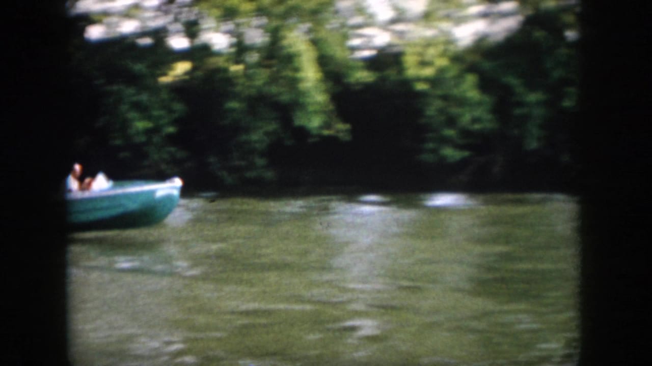 A home-movie frame catches the motorboat near the edge of the shot, with rippled water and dense riverside trees.