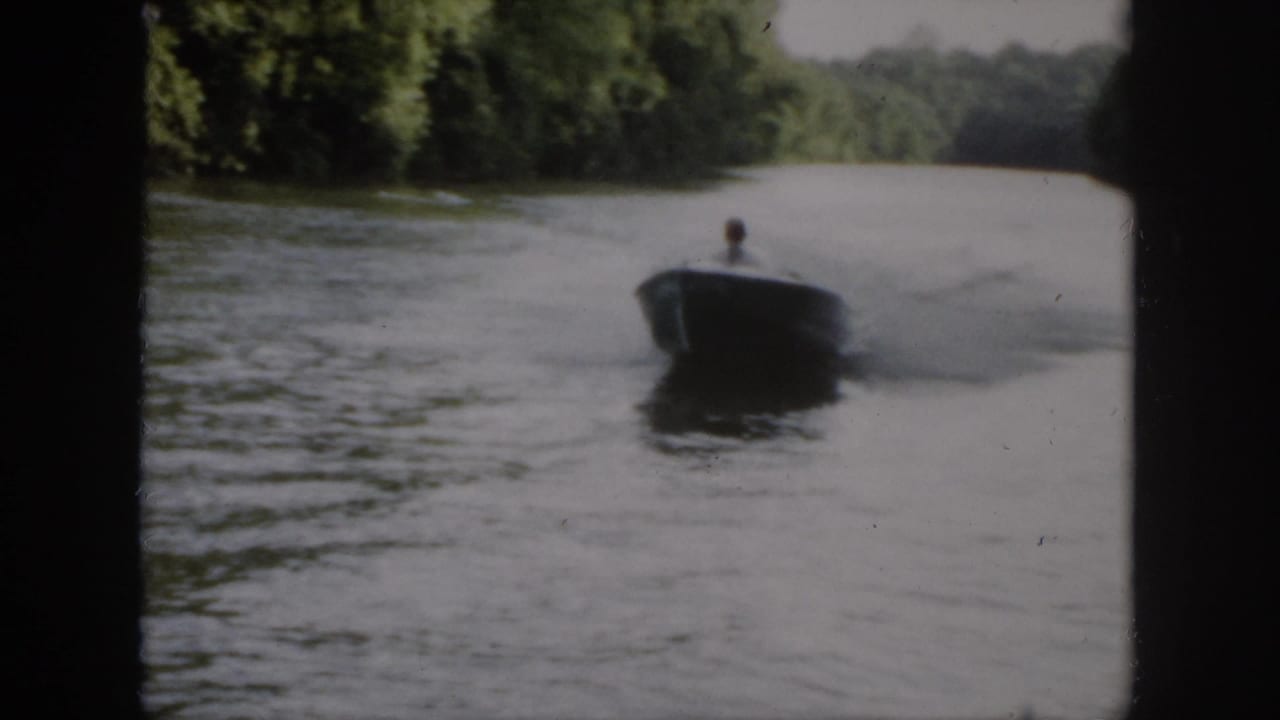 In 1958 Virginia home-movie footage, a small motorboat approaches along a tree-lined waterway with one adult visible aboard.