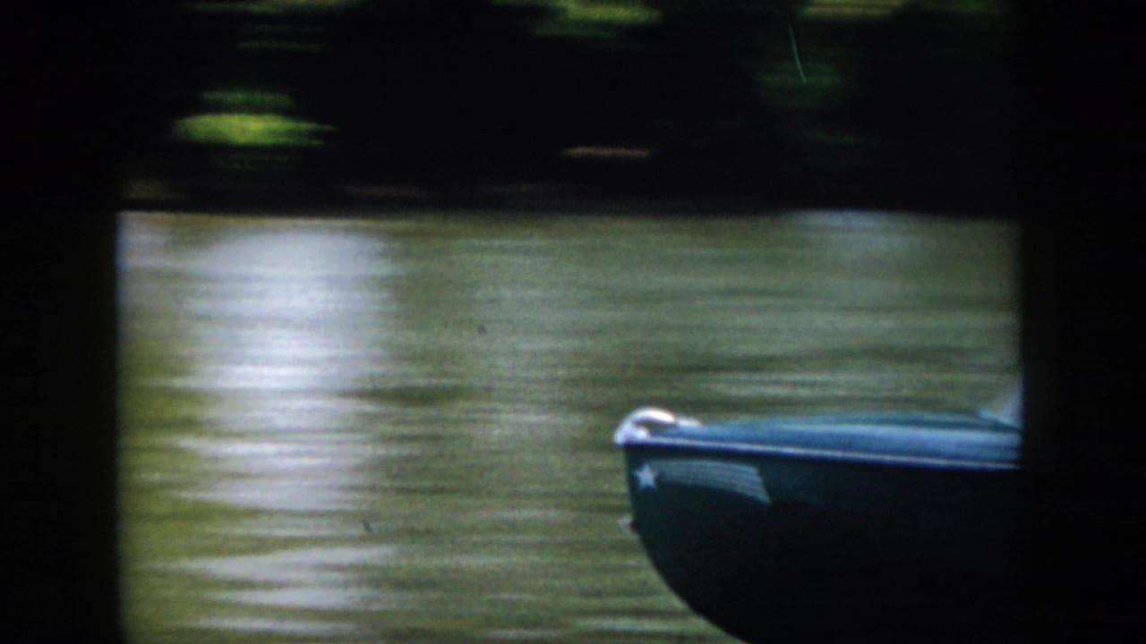 A small blue motorboat passes near the camera on a wooded Virginia waterway, with only the bow and side clearly visible.