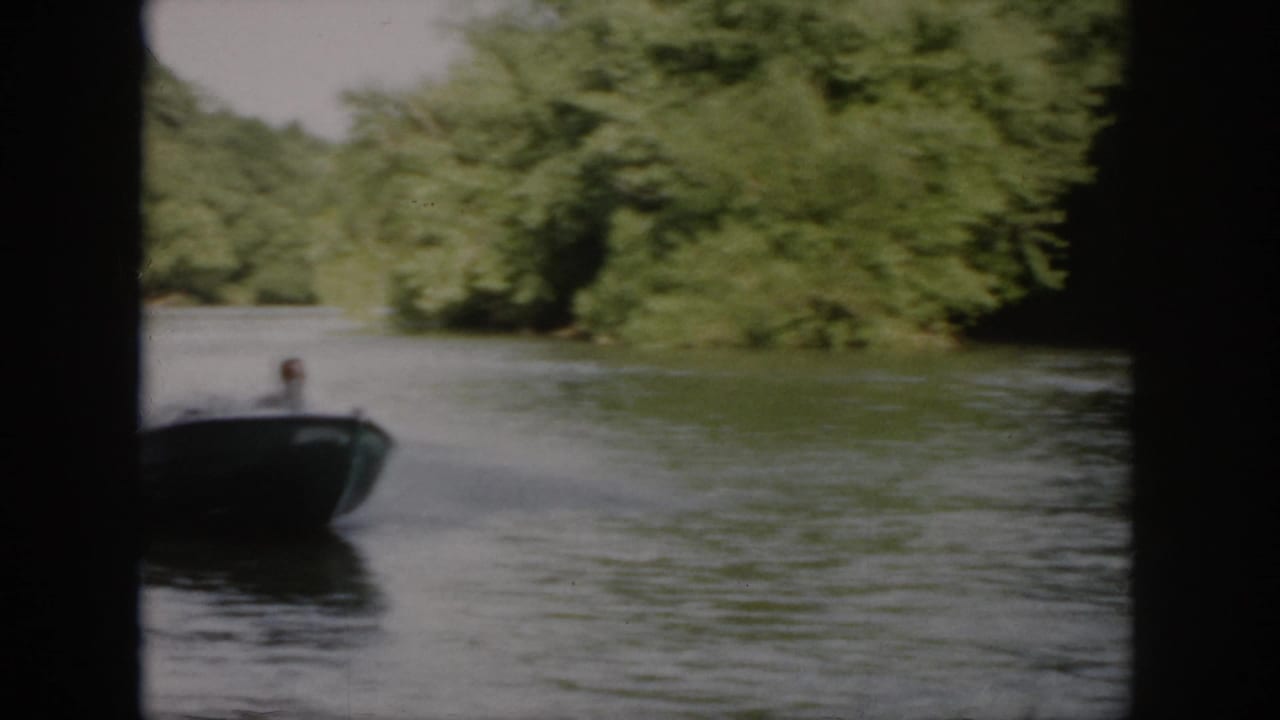 Small speedboat approaches on a wooded Virginia waterway in 1958 home-movie footage, with the operator only faintly visible.