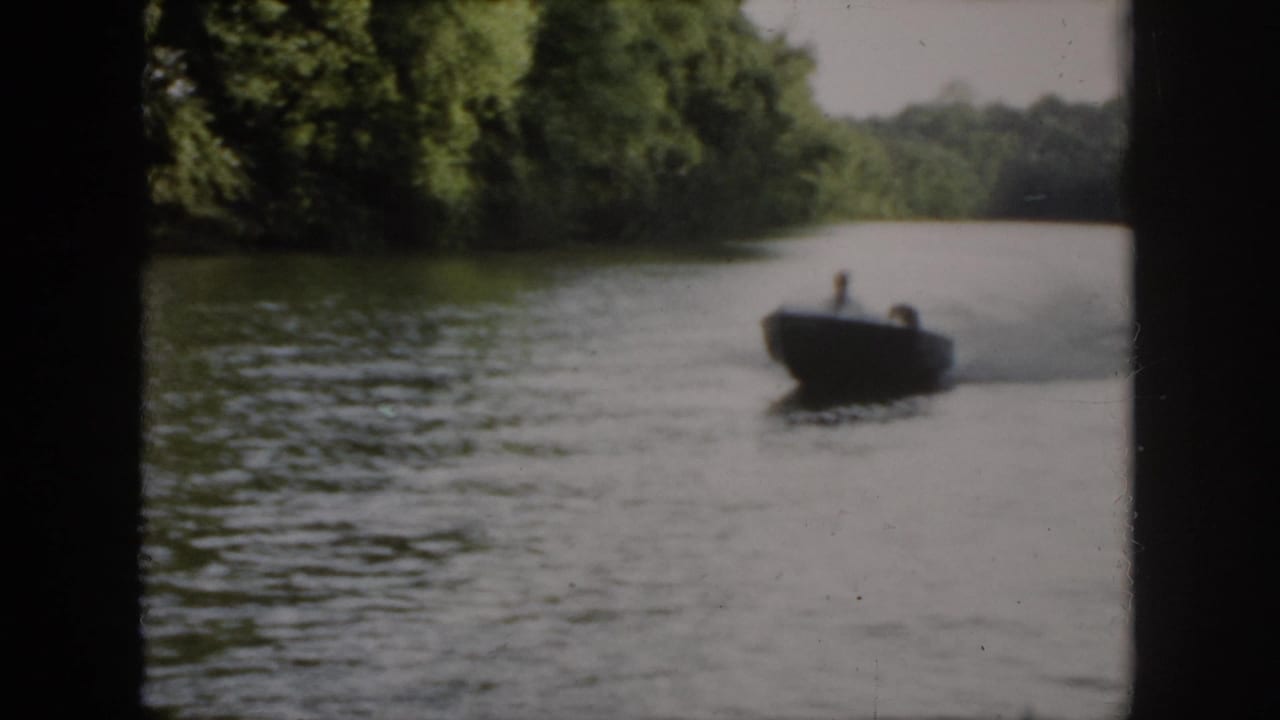 Speedboat traveling across the right side of a tree-lined river or lake.