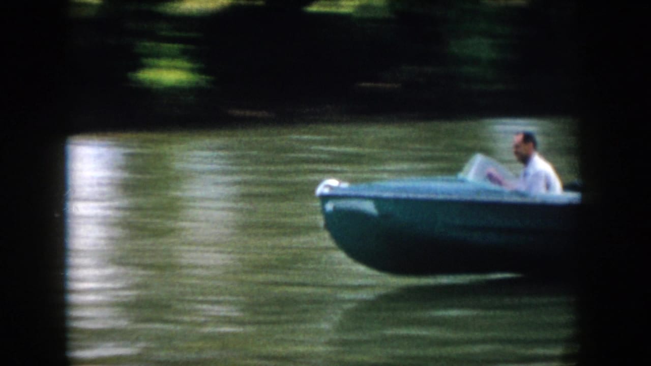 Closer side view of a man steering a blue speedboat on a Virginia body of water in 1958 home-movie footage.