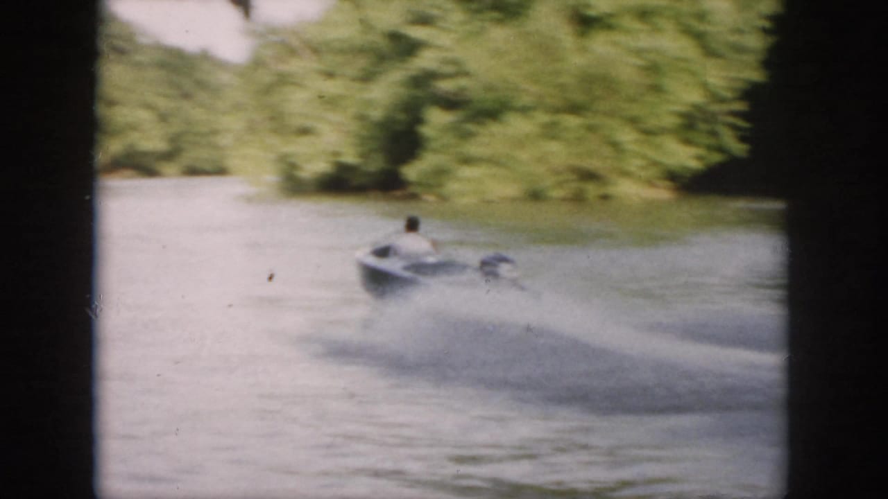 The speedboat races away across a wooded Virginia waterway, trailing a wide spray wake in 1958 8mm footage.
