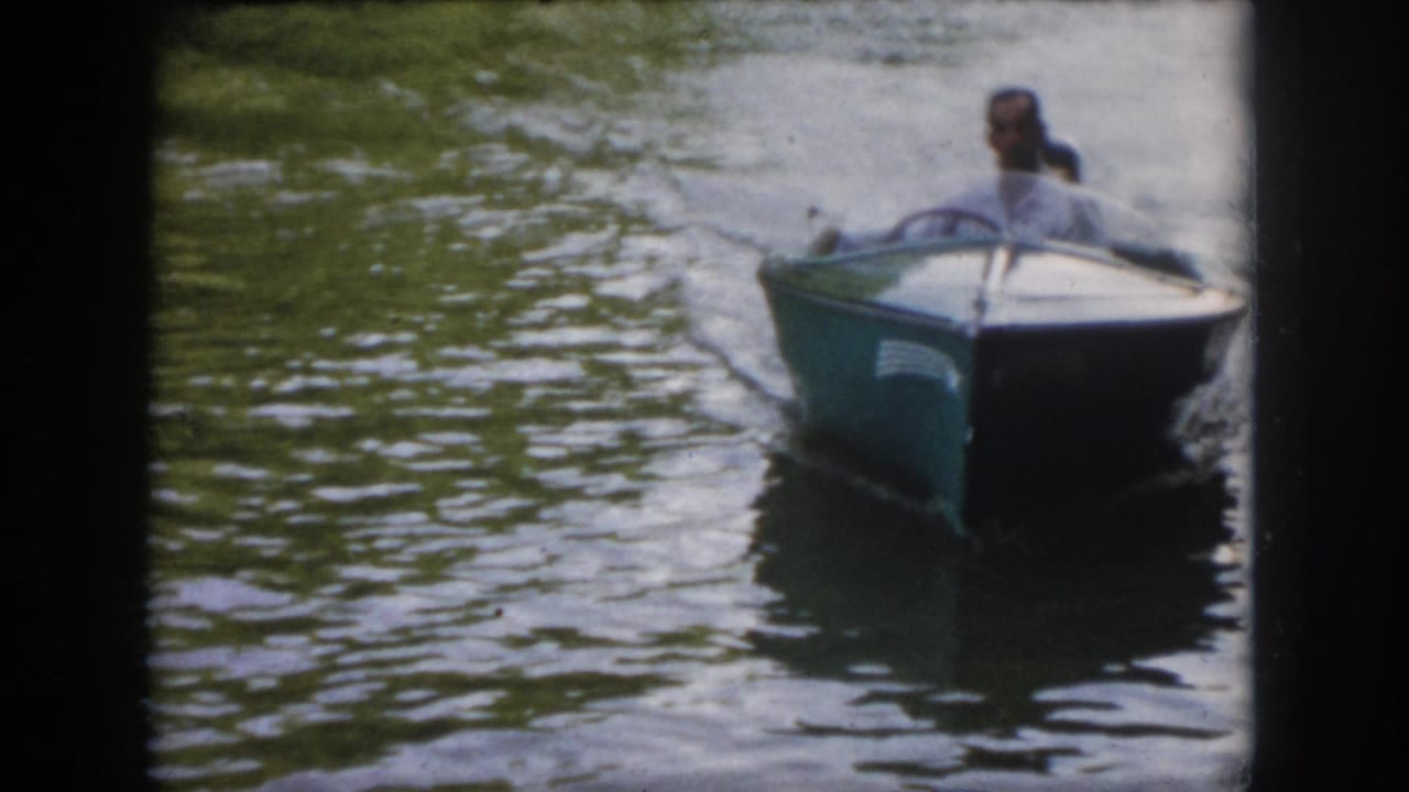 A man in a light shirt steers a small speedboat toward the camera on a Virginia river in this 1958 8mm home movie frame.