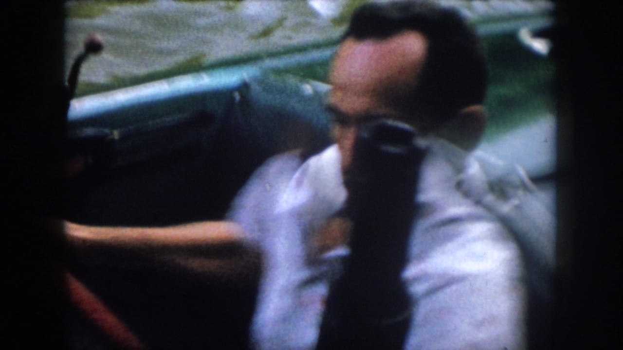 Close 1958 Virginia home-movie view of a man steering or seated at a small motorboat, with the river visible in the background.