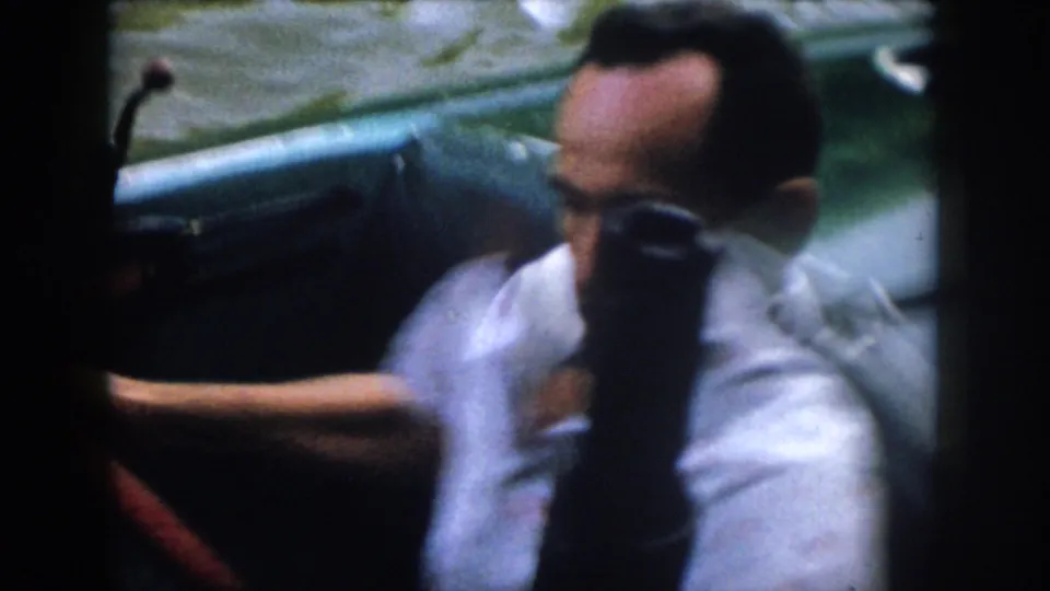 Close 1958 Virginia home-movie view of a man steering or seated at a small motorboat, with the river visible in the background.