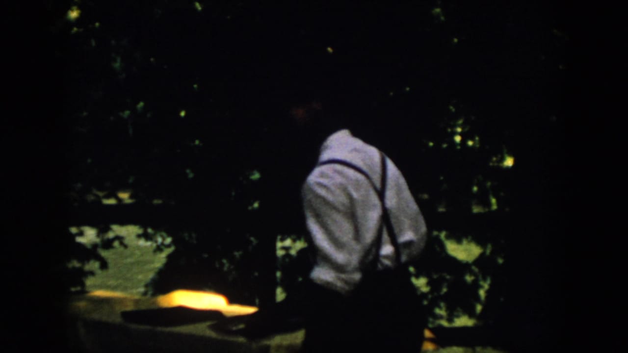 In 1958 Virginia home-movie footage, an adult man in suspenders is seen from behind near a dark wooded waterfront.