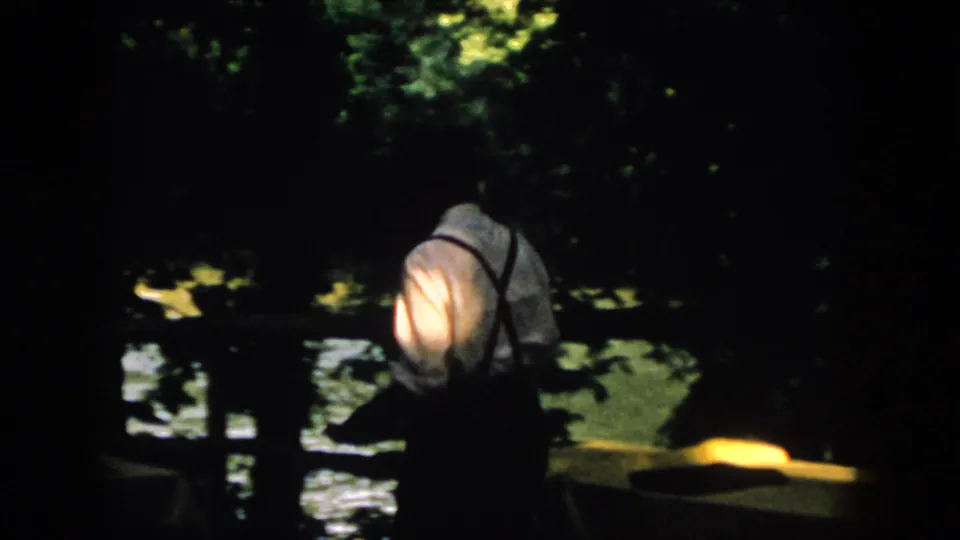 The man continues along the shadowed Virginia waterfront, his pale shirt catching warm light amid trees and water reflections.