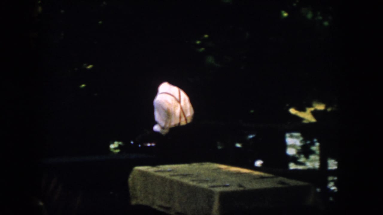 The man appears partly turned or bending near a low ledge at the dark waterfront, with the 8mm frame dominated by shadow.
