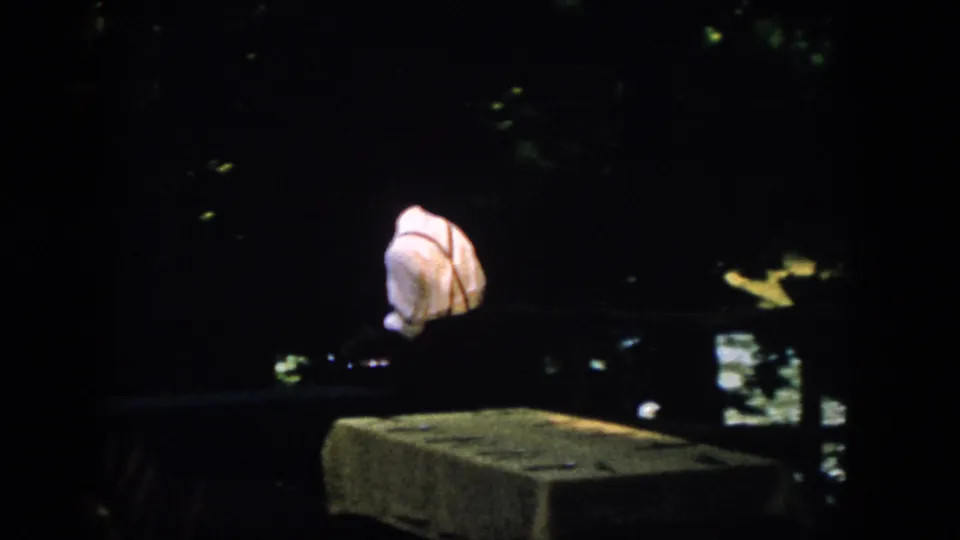 The man appears partly turned or bending near a low ledge at the dark waterfront, with the 8mm frame dominated by shadow.
