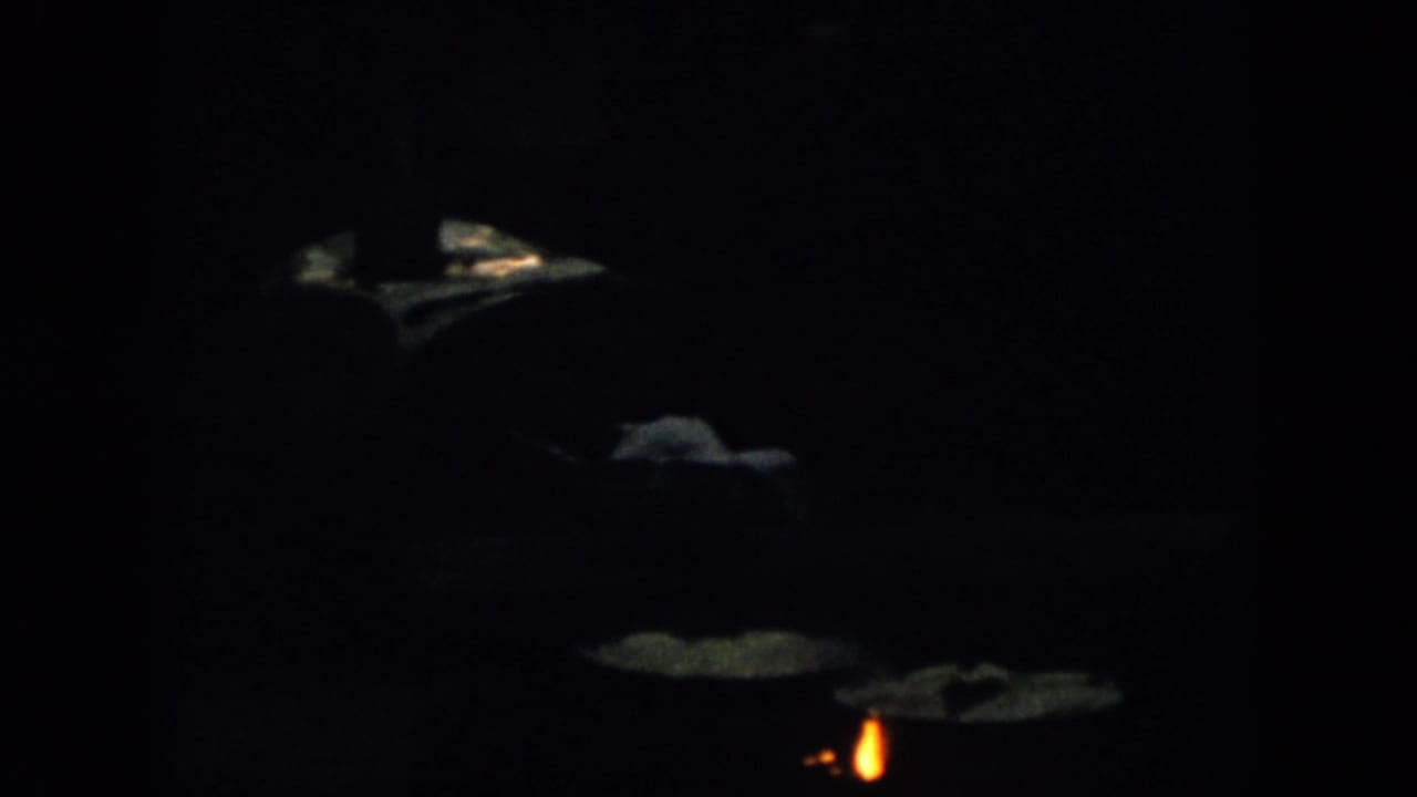 Dark 1958 Virginia home-movie frame with small orange flames and faint surrounding shapes, likely part of the fire-lit porch sequence.