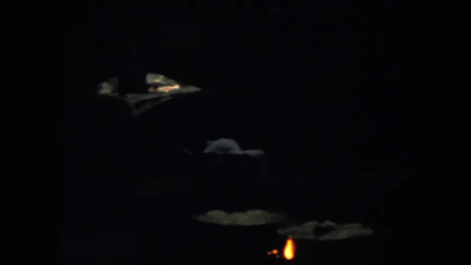 Dark 1958 Virginia home-movie frame with small orange flames and faint surrounding shapes, likely part of the fire-lit porch sequence.