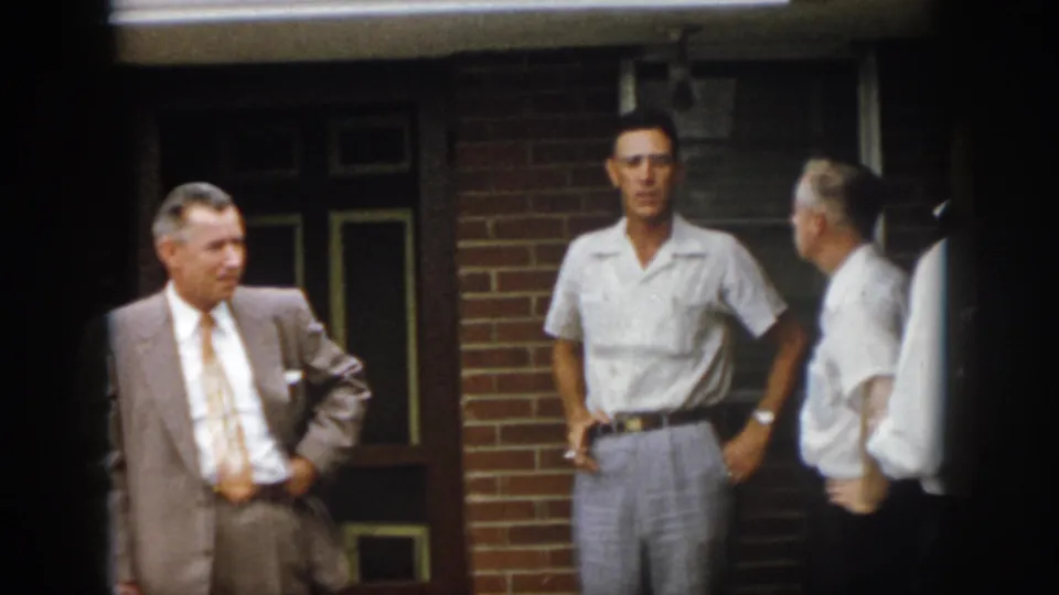 1958 Virginia porch scene with a suited man and two casually dressed men standing near a brick wall and dark doorway.