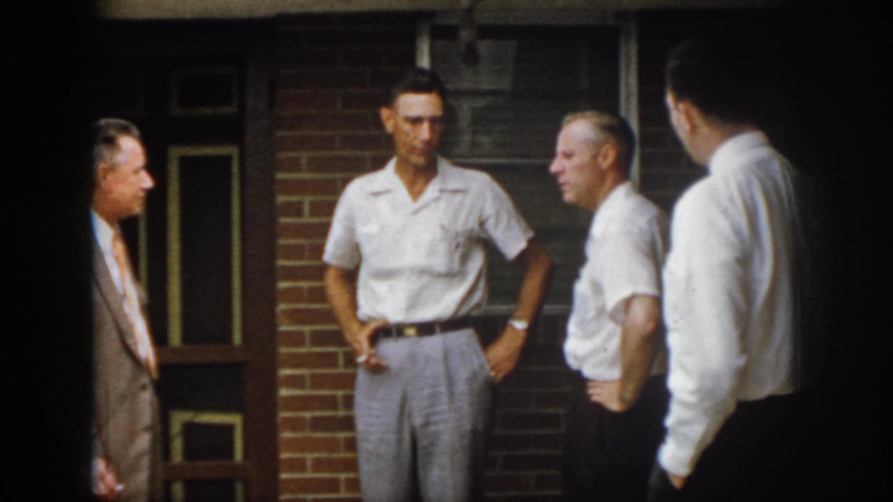 In 1958 Virginia home-movie footage, four adult men appear in conversation outside a brick building with windows and a doorway.