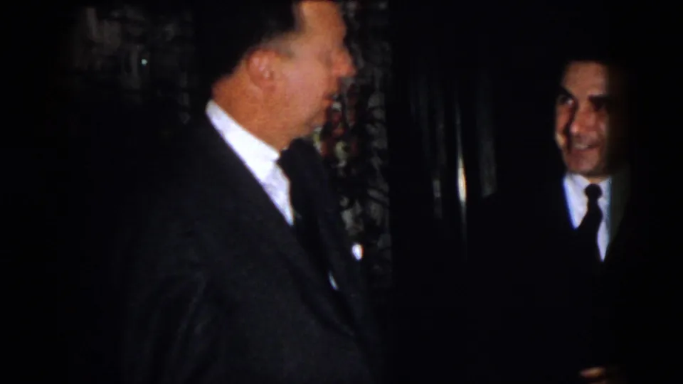 1958 Virginia frame showing two adult men in suits facing each other in low light during a formal indoor social moment.