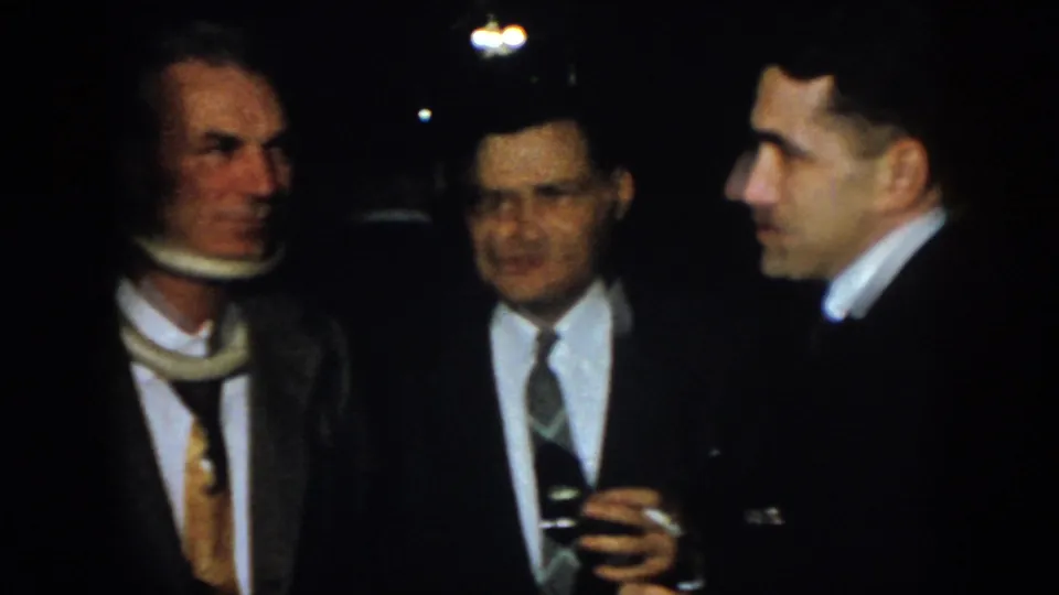 1958 Virginia home-movie frame of suited men conversing, with one visible man wearing a neck brace or medical support.
