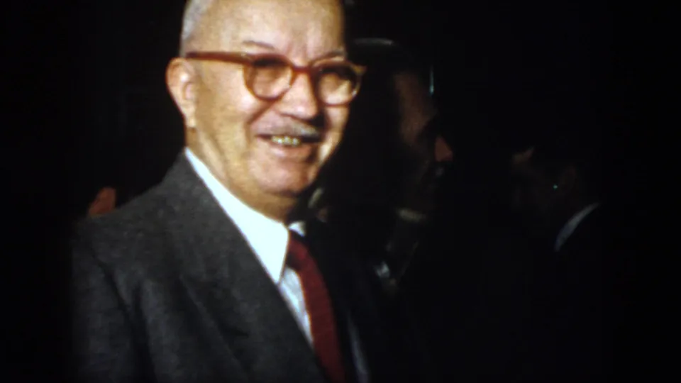 1958 Virginia frame showing an older suited man with glasses smiling near the camera while others remain in shadow.
