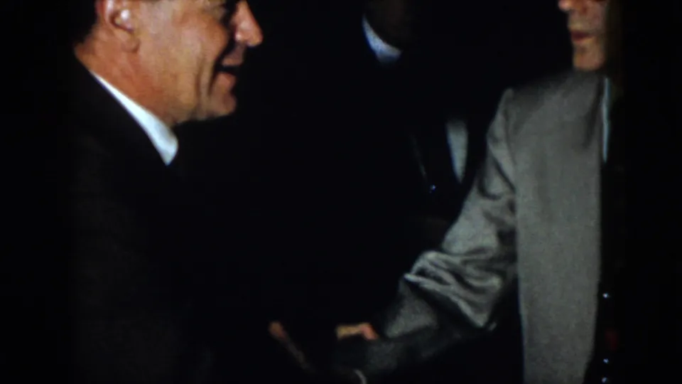 1958 Virginia 8mm frame with a close side view of adult men at a formal indoor gathering, including one light-colored jacket.