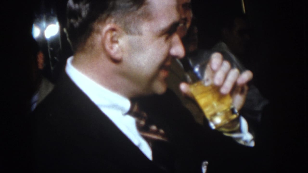 Man in a dark suit drinks from a glass in profile.