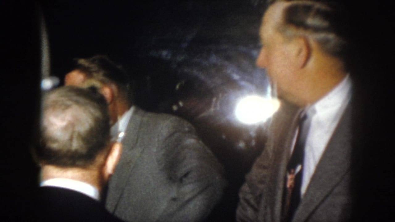 1958 Virginia home-movie frame showing suited men in close conversation at a dark nighttime gathering with strong light glare.