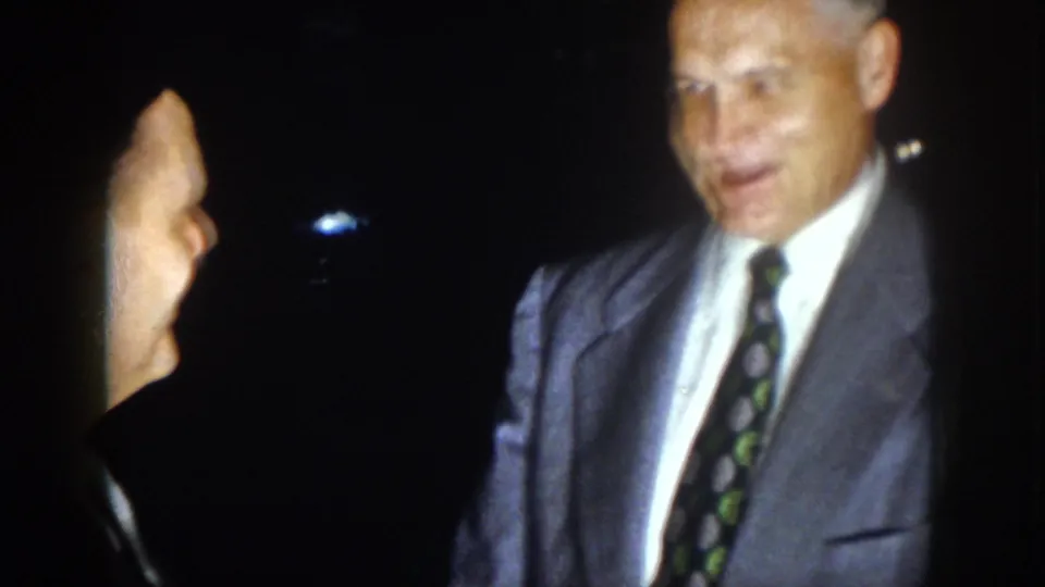 A formally dressed man with graying hair faces another man in profile during the 1958 Virginia nighttime scene.