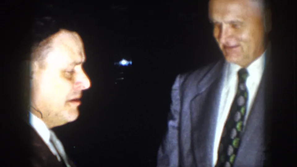 A man in profile and another suited man remain in close conversation in the 1958 Virginia home-movie footage.