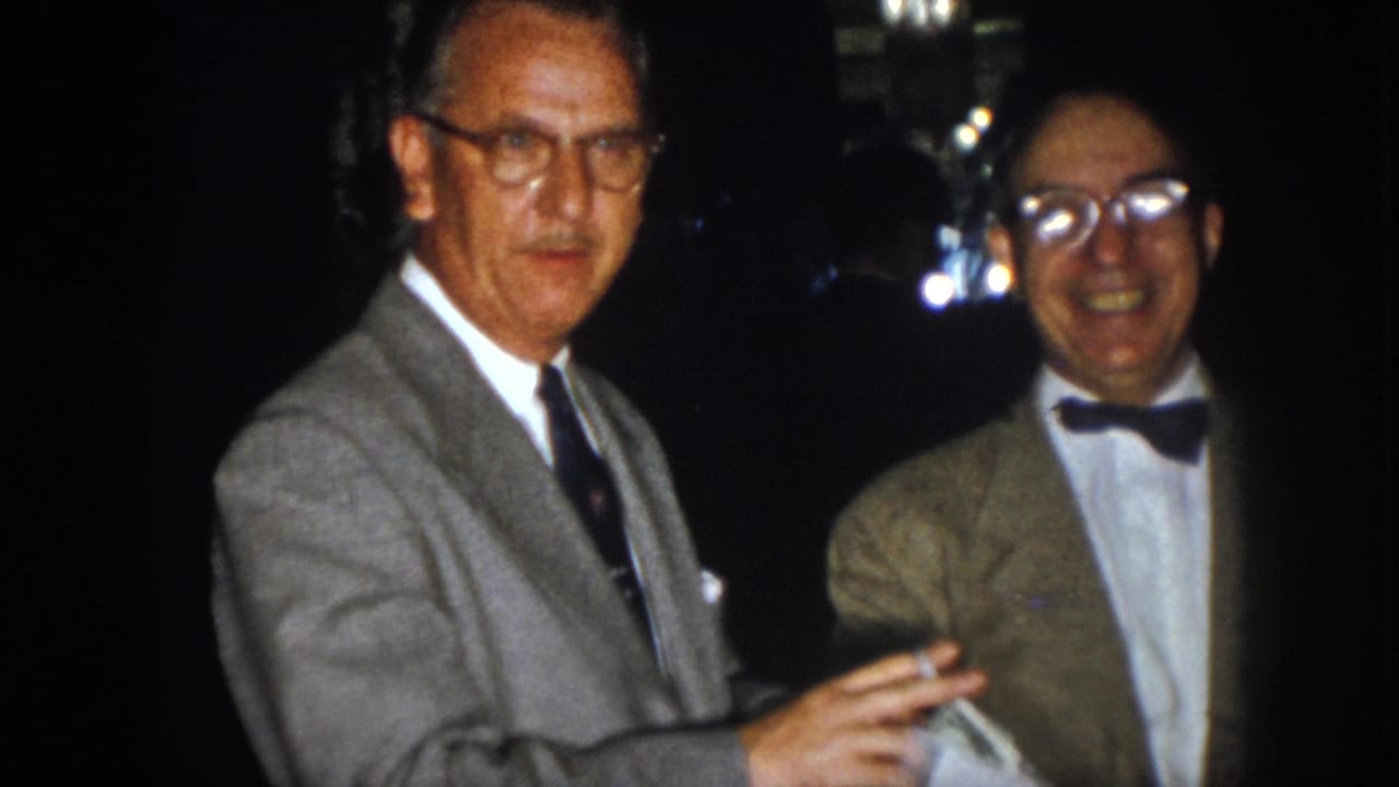 Two older men face the camera at night, one in a gray suit and one in a bow tie.