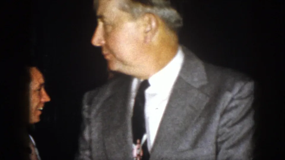 1958 Virginia 8mm frame with a gray-suited adult man in profile and a second smiling man partly visible behind him.