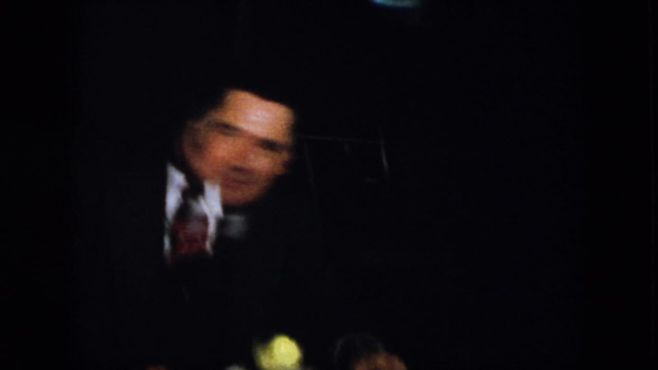 Man in a dark suit and tie partly visible in dim light.