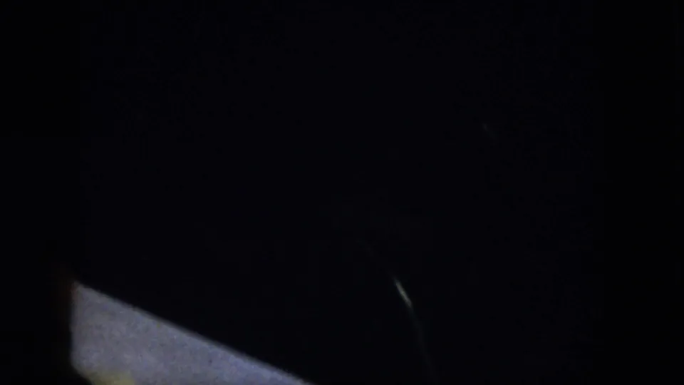 Dim home-movie frame from the Virginia dinner scene, with only a vague figure and tabletop area visible.