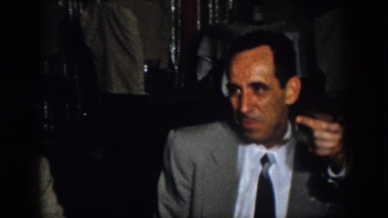In the final 1958 Virginia frame, an adult man in a gray suit looks off-camera while another person gestures toward him in the dim private dining or restaurant setting.
