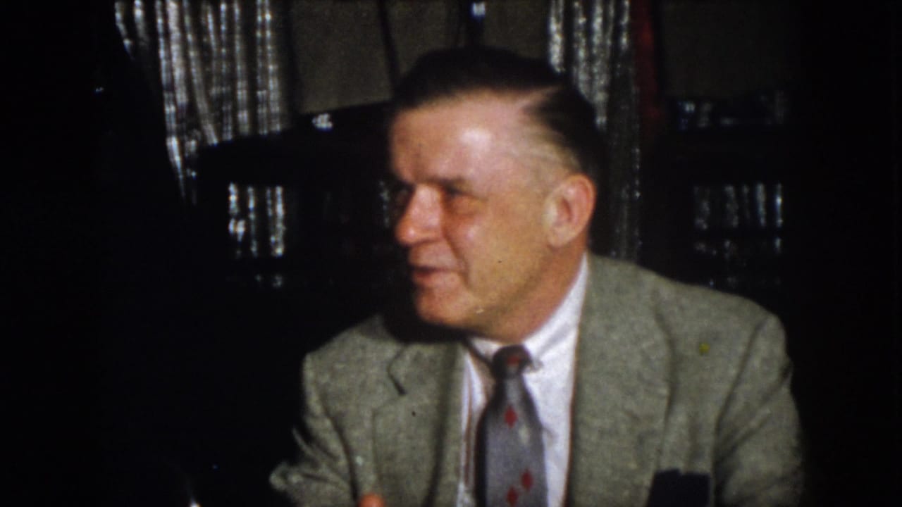 Virginia 1958 home-movie frame of a seated man in a light jacket and patterned tie turning during conversation.