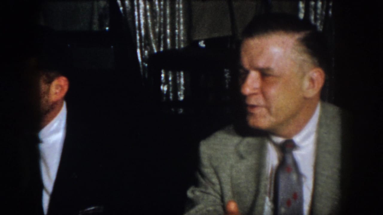 Virginia 1958 frame showing suited men seated in a dim private interior, one partly obscured by shadow.