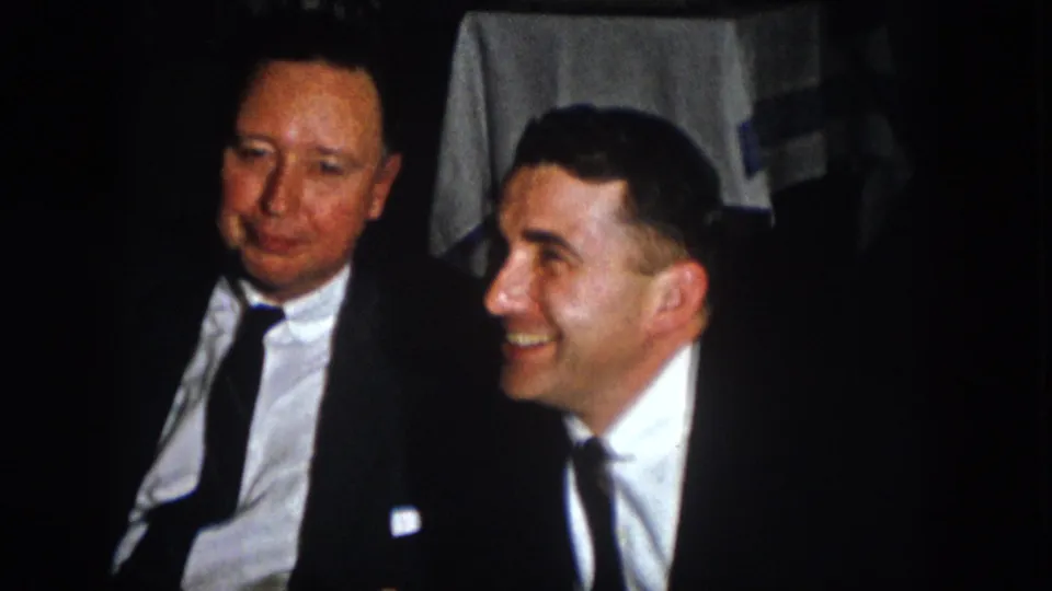 At the Virginia banquet, two men in formal suits sit close together as one smiles broadly.