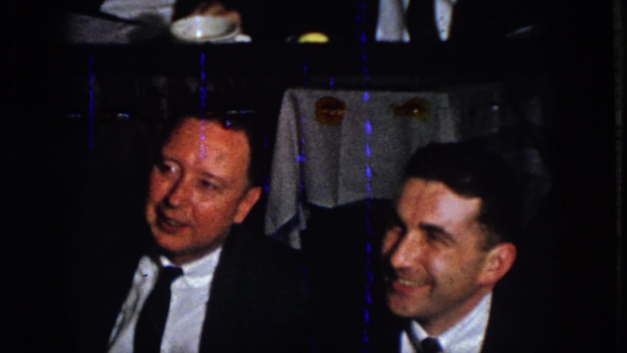 Two formally dressed men smile at a dimly lit banquet table in 1958 Virginia home-movie footage.