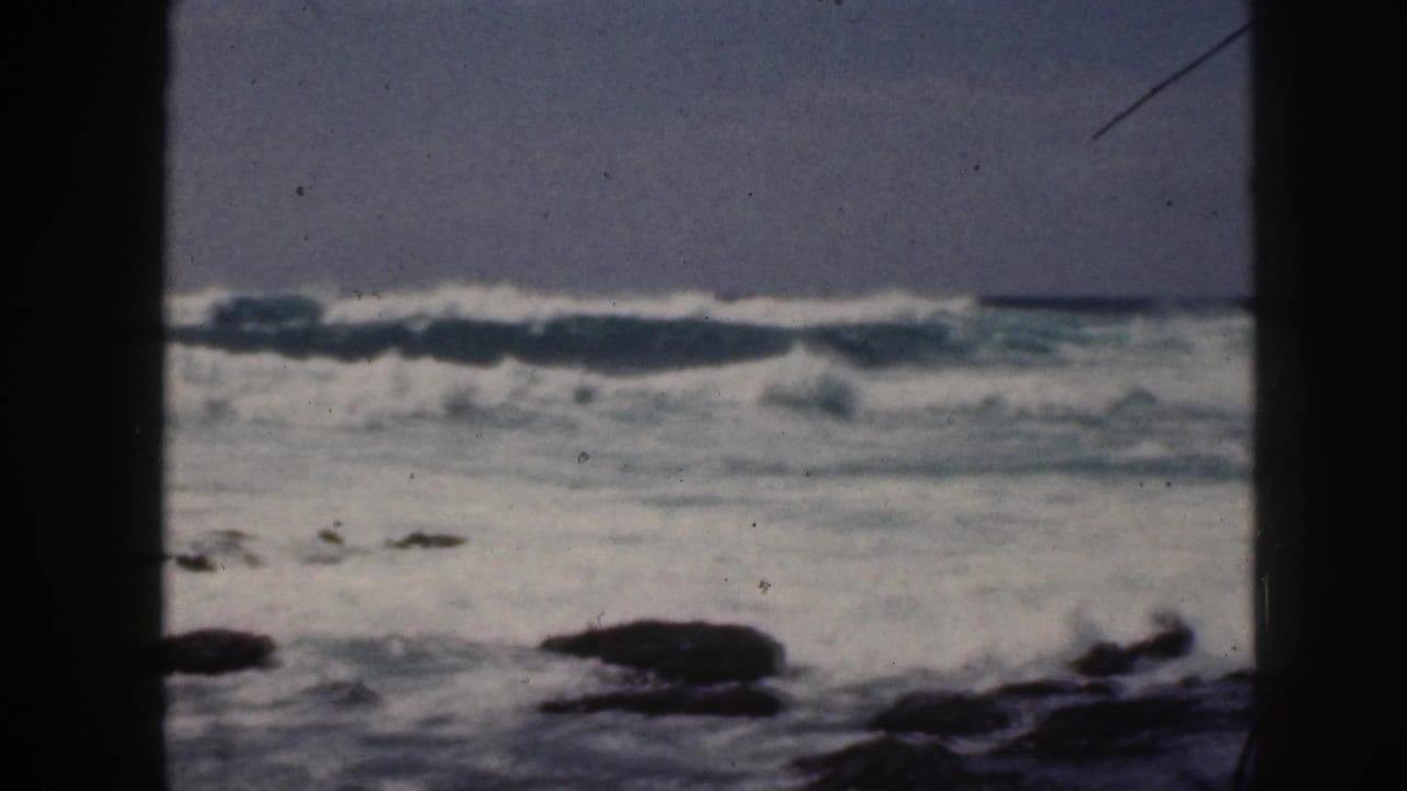 White surf and dark rocks viewed through a shadowed vertical divider.