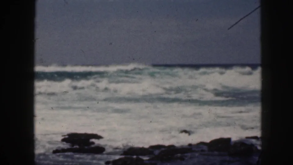 1959 Hawaii 8mm frame showing waves cresting along a rocky Pacific shoreline with soft focus and faded color.