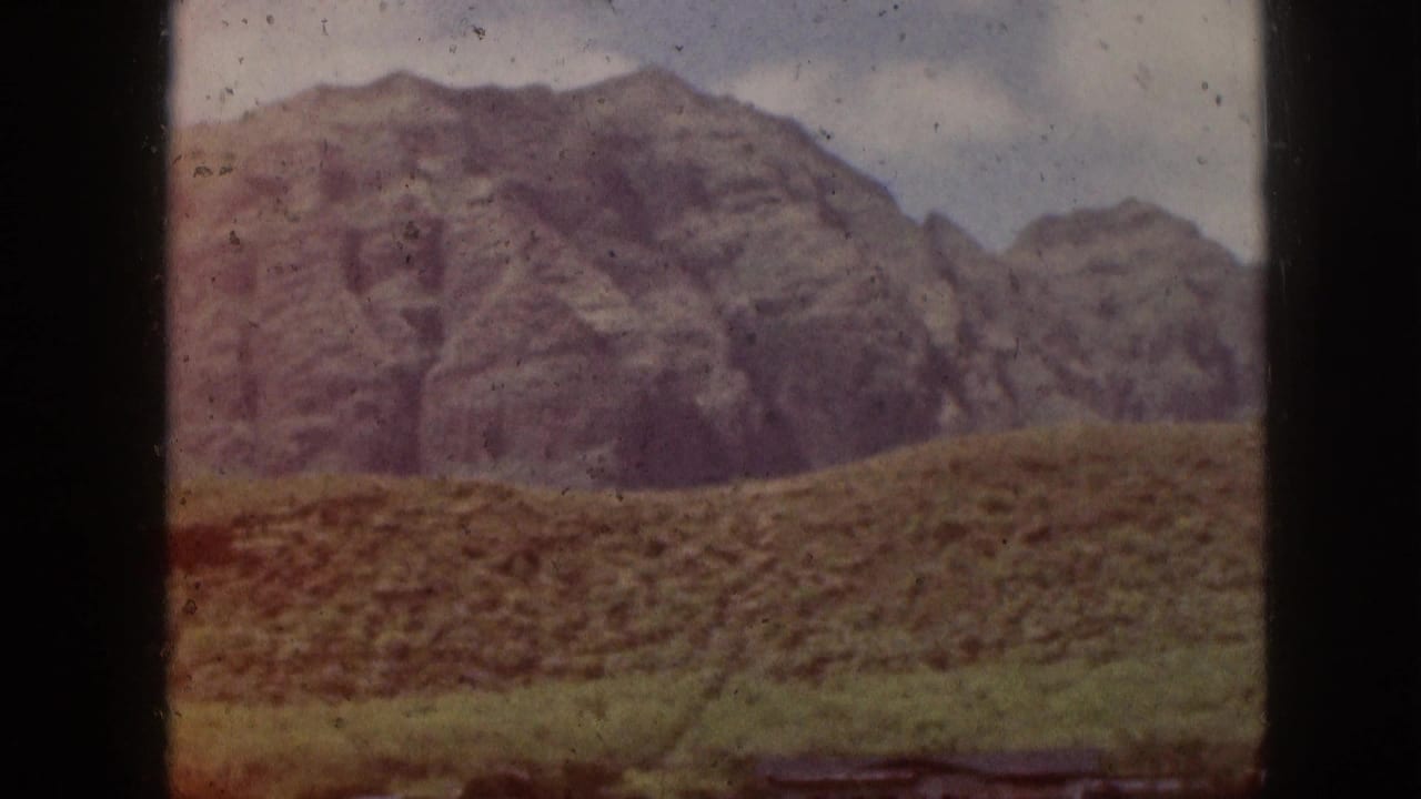 Rocky mountain ridge beyond green hills, seen through dark vertical frame bars.