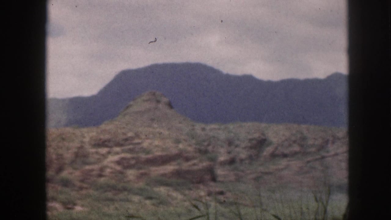 1959 Hawaii 8mm frame showing muted mountain terrain, rocky foreground, sparse vegetation, and a dark window frame.
