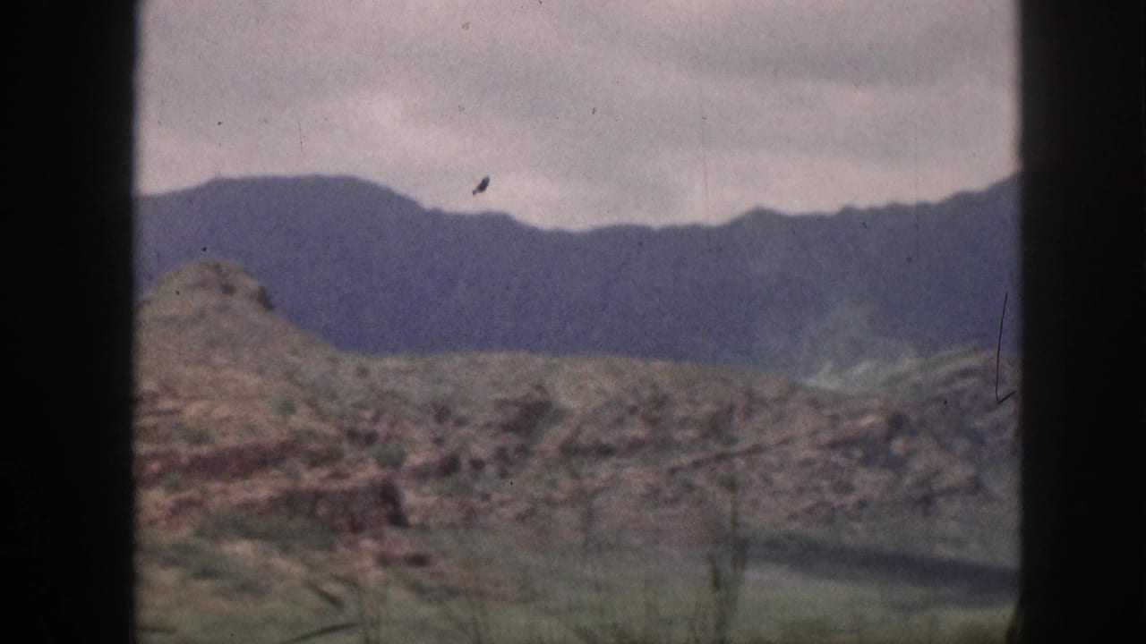 Rocky hill and distant dark mountain ridge divided by a vertical window frame.