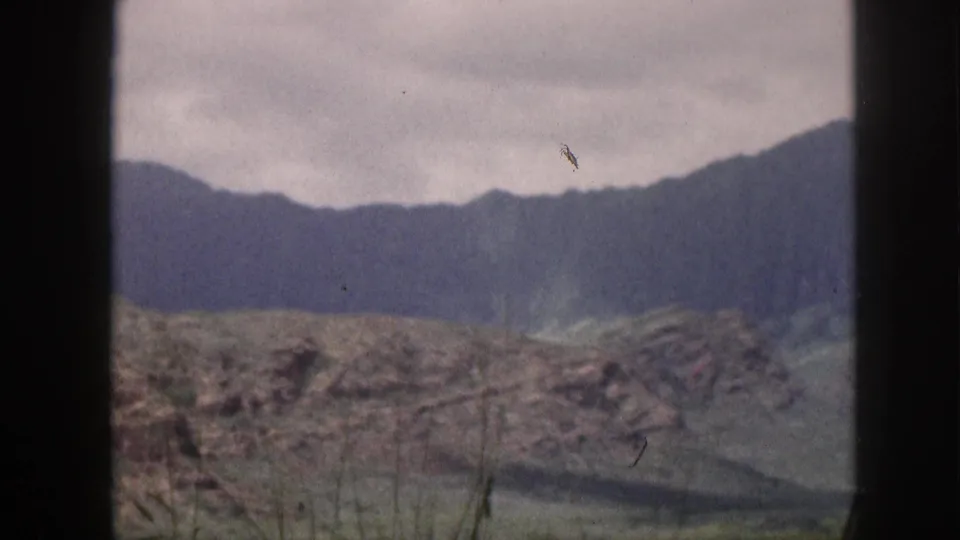 1959 Hawaii 8mm frame showing a soft, overcast mountain slope behind rocky scrub terrain and dark window edges.