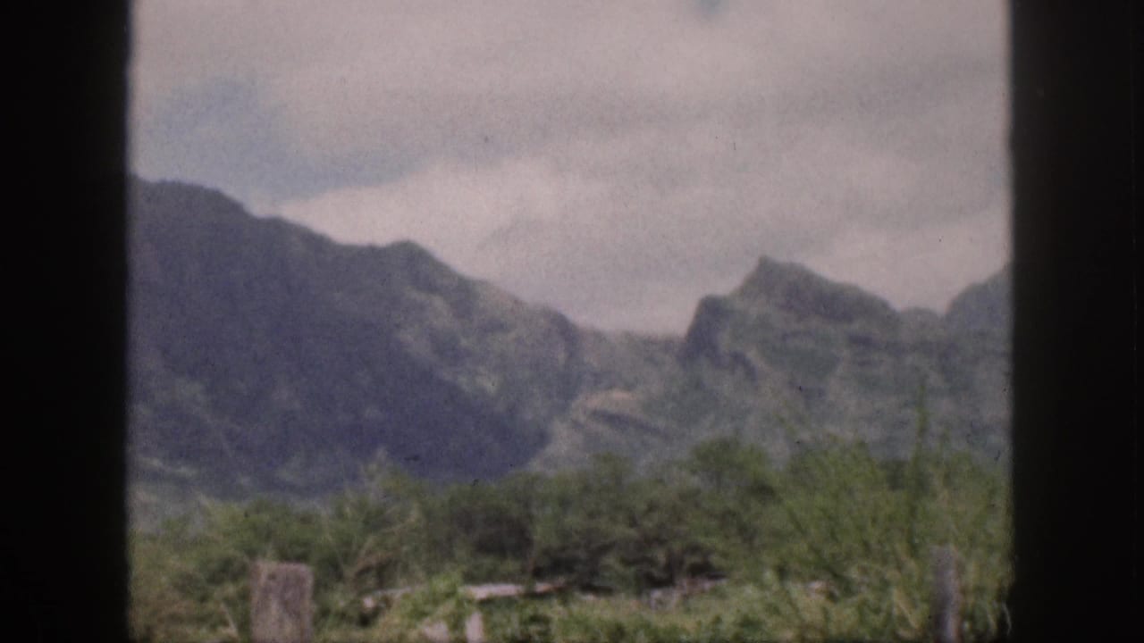 Cloudy sky hangs over rugged mountains and low green brush behind a dark central frame bar.