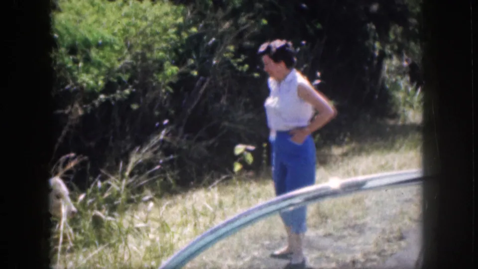 A woman in blue pants stands with hands at her waist while the calf remains partly visible in the grass nearby.