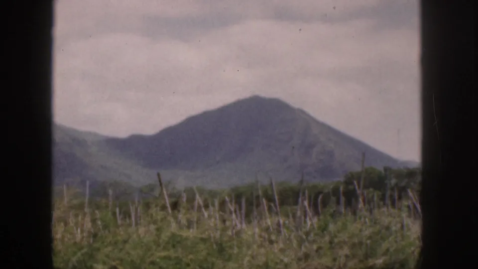 1959 Hawaii home-movie view of a green mountain and foreground vegetation through a dark window or vehicle frame.